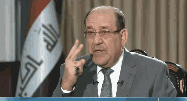 a man in a suit and tie is sitting in front of a flag that says ' iraqi ' on it