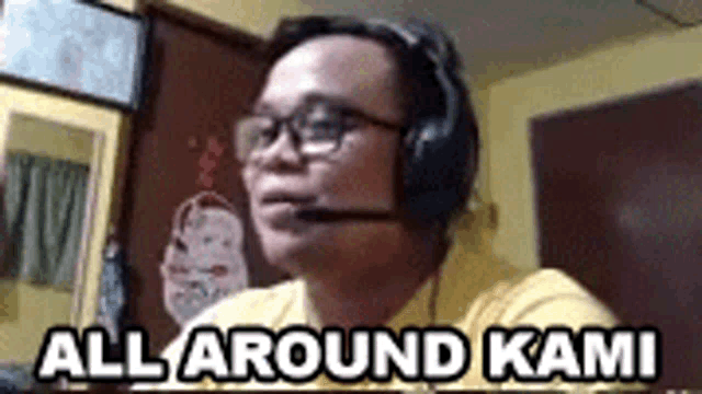 a man wearing headphones and glasses is sitting in front of a computer screen and says `` all around kami '' .