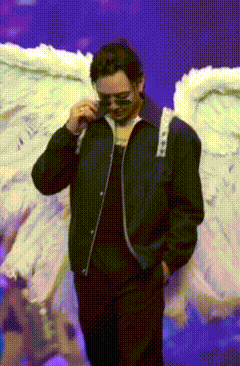a man wearing sunglasses and a black jacket is standing in front of white angel wings