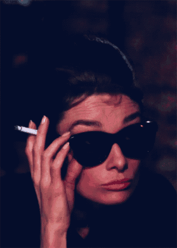 a woman wearing sunglasses holds a cigarette in her right hand