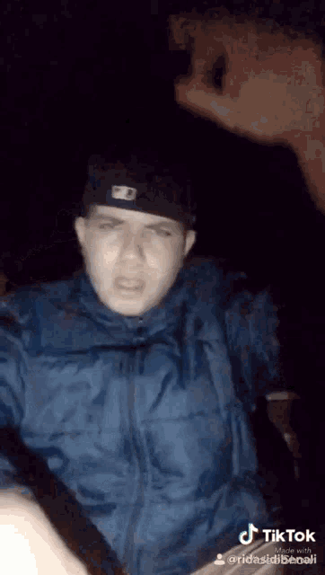 a man wearing a hat and a blue jacket is making a funny face in a tik tok video
