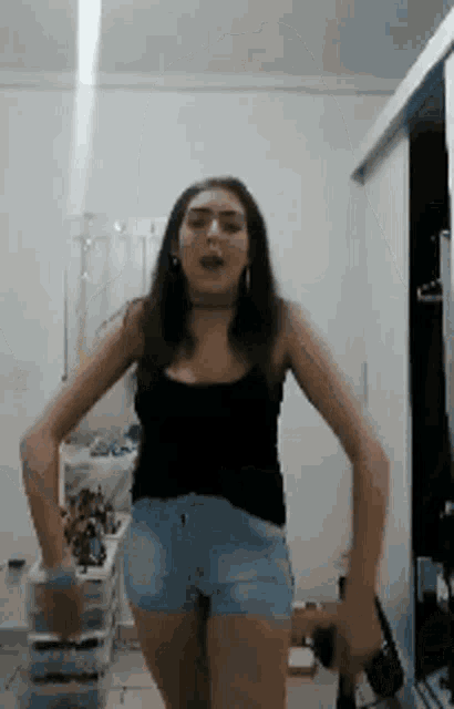 a woman in shorts and a black tank top is dancing in a room