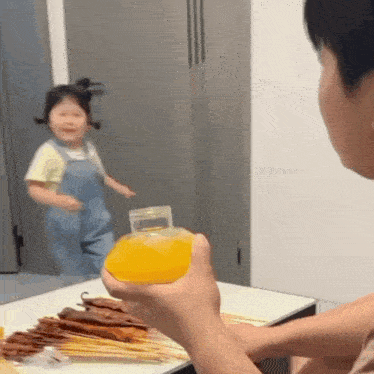 a man is holding a bottle of orange juice in front of a little girl