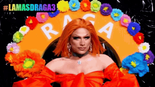 a drag queen in a red dress is surrounded by colorful flowers and a sign that says " lamasdraga3 "