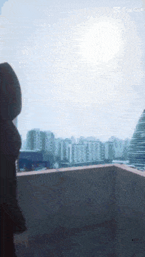 a woman stands on a balcony overlooking a city and the sun is shining through the window