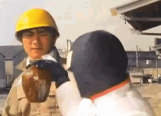 a man wearing a hard hat is holding a bottle in his hand while another man wearing a mask looks on .