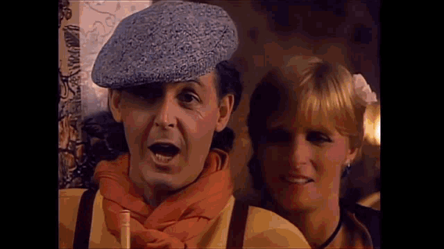 a man and a woman are standing next to each other . the man is wearing a hat and scarf .