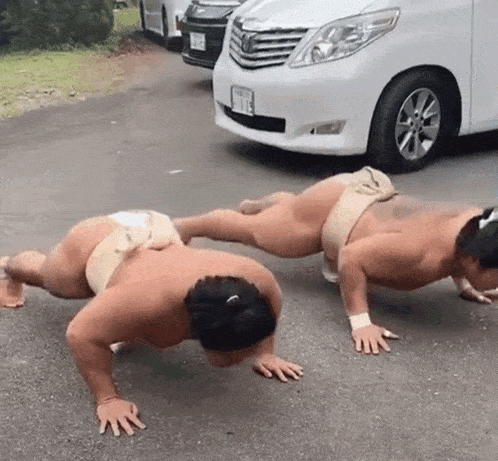 two sumo wrestlers are doing push ups on the street