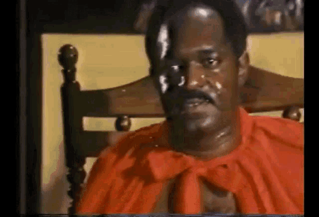 a man in a red shirt is sitting in a chair with a red cape on his head .