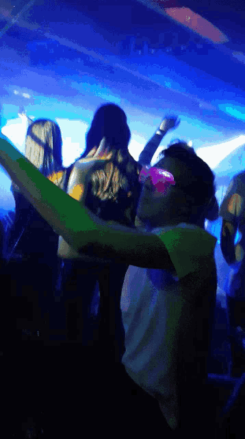 a man wearing pink sunglasses and a green shirt is dancing in a club