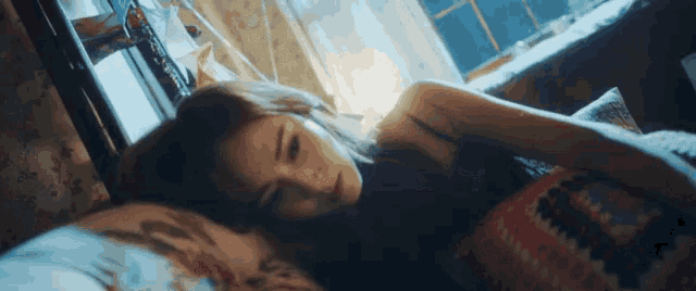 a woman is laying in bed with her head on a pillow looking at the camera .