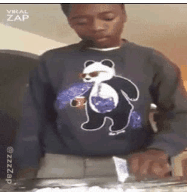 a young man wearing a panda bear sweater is holding a cup of soda .