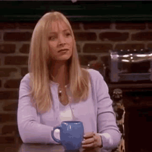 a woman is sitting at a table holding a blue coffee mug .