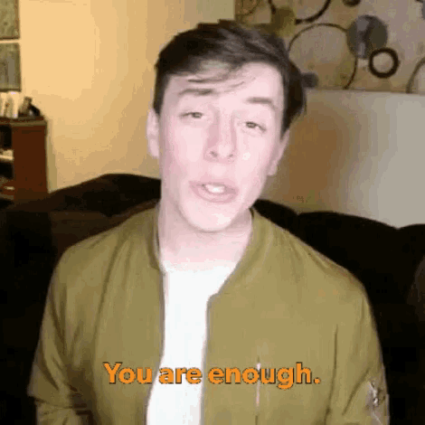 a man in a green jacket is saying `` you are enough '' while standing in front of a couch .