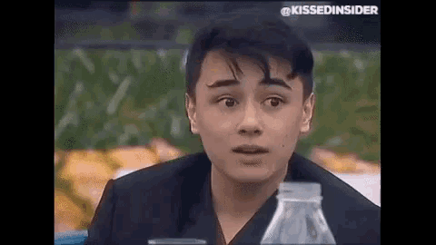 a young man is sitting at a table with a bottle of water and making a surprised face .