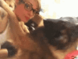 a woman wearing glasses is petting a dog while sitting on a bed .