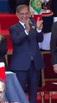 a man in a suit and tie applauds while standing in front of a crowd
