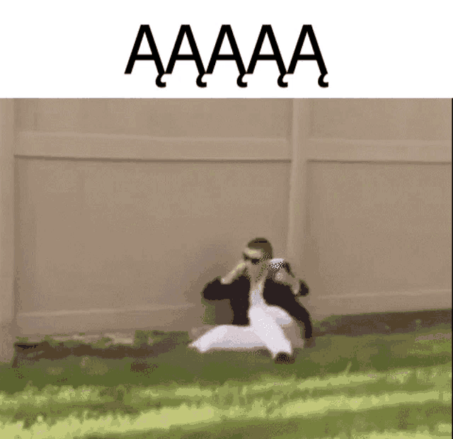 a man is sitting on the ground in front of a fence with the words aaaa written above him .