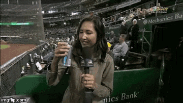 a woman is holding a can of soda in front of a mechanics bank sign