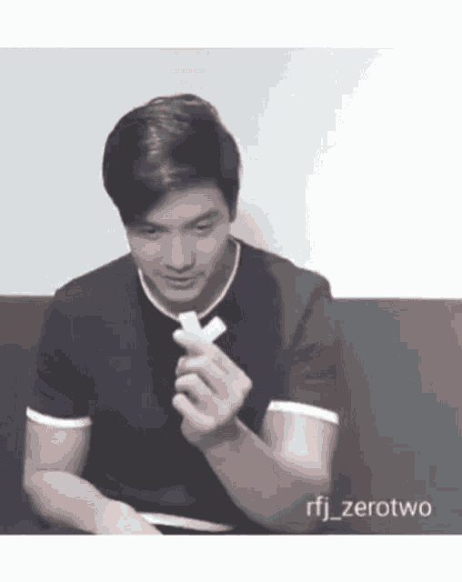 a man in a black shirt is sitting on a couch holding a piece of cheese in his hand .