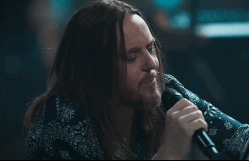 a man with long hair singing into a microphone