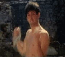 a man without a shirt is standing in front of a stone wall with his hands in the air .