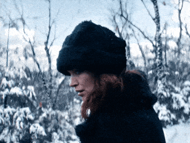 a woman wearing a black fur hat and a black coat stands in the snow