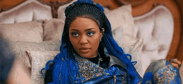 a woman with blue hair is sitting on a bed in a room .