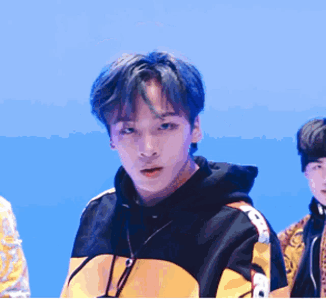 a young man with blue hair is wearing a black and yellow hoodie .