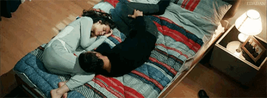 a man and a woman are laying on a bed with a picture on the nightstand that says ' idadan '