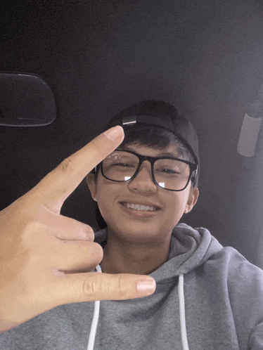 a young man wearing glasses and a black hat is giving the peace sign