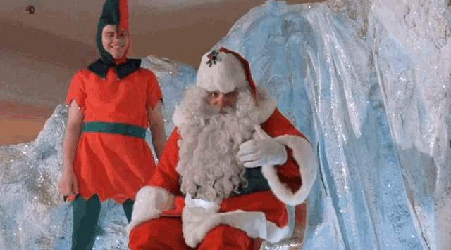 a man in an elf costume stands next to a man in a santa suit