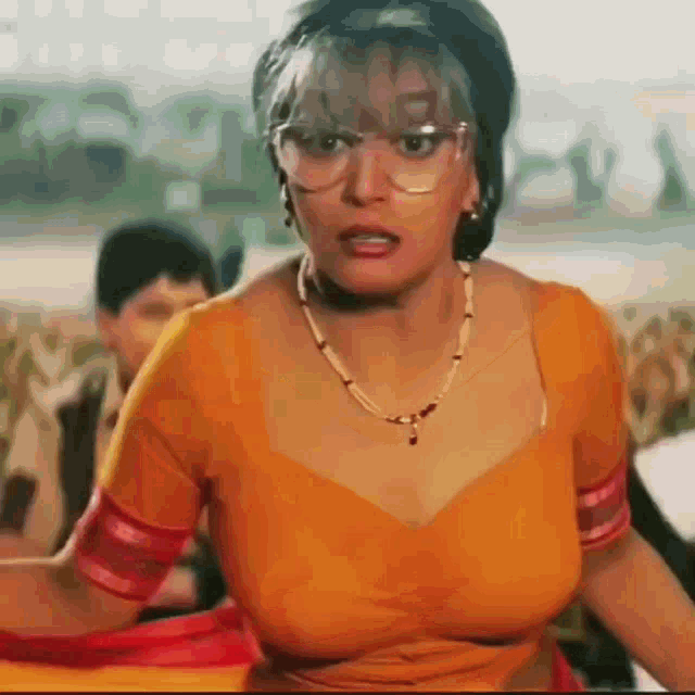 a woman wearing glasses and a yellow top is sitting on a couch with a boy in the background .