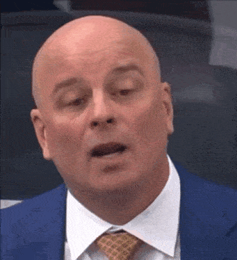 a bald man in a suit and tie is sitting in a chair .