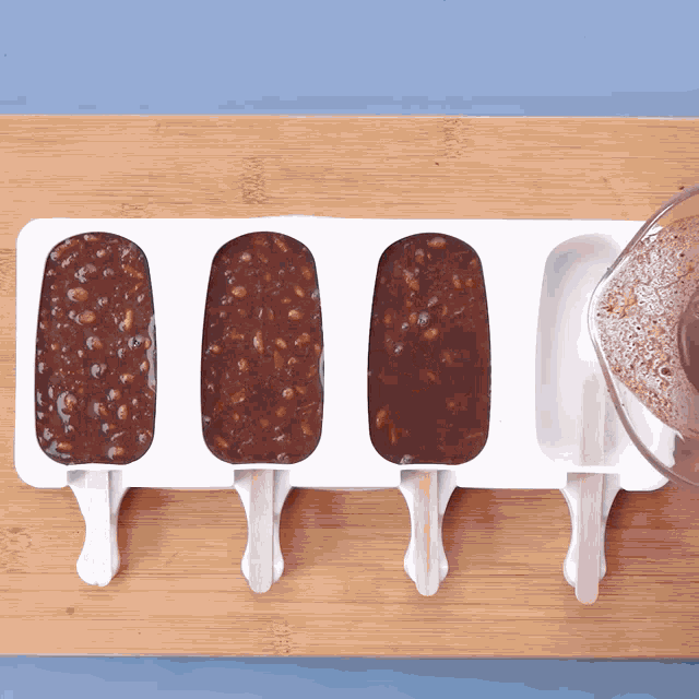 four popsicle molds filled with chocolate and nuts on a wooden cutting board