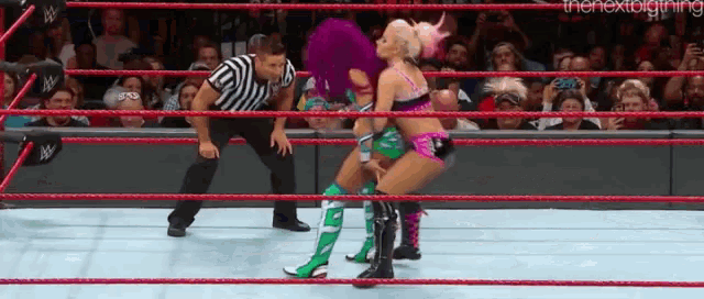 two women are wrestling in a ring with a referee in the background .