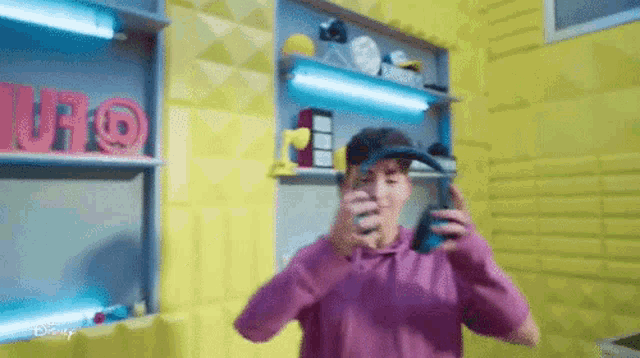 a man in a pink hoodie is holding a cell phone in front of a yellow wall .