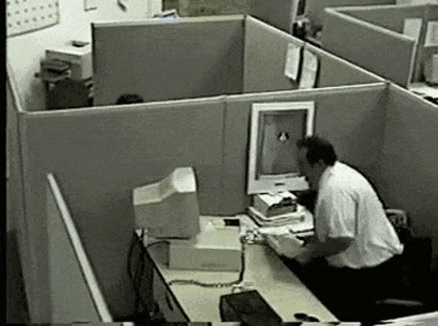 a man sits at a desk in an office cubicle with a computer