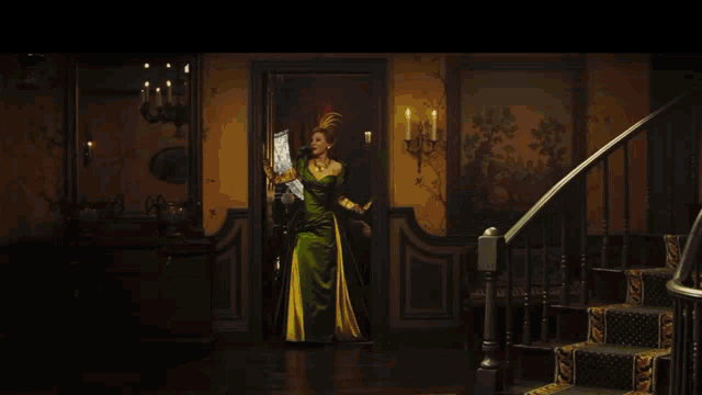 a woman in a green dress is standing in a room with candles on the wall