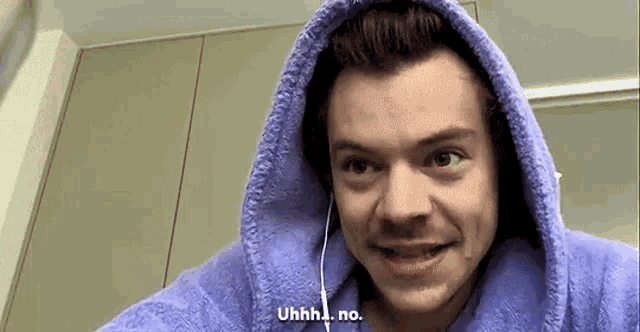 harry styles is wearing a purple robe with a hood and earphones on his head .