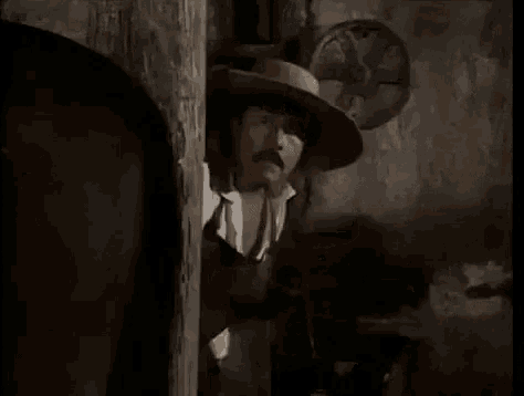 a man wearing a cowboy hat is peeking out from behind a wall .