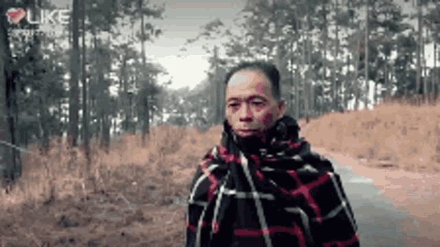 a man with a scarf around his neck is walking down a road in the woods ..