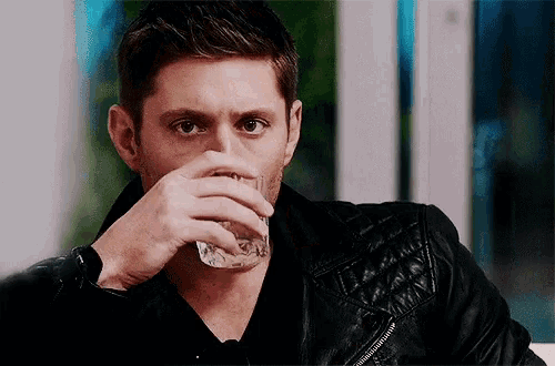 a man in a leather jacket drinking from a glass