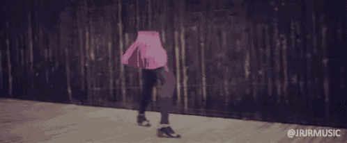 a woman in a pink skirt and purple pants is walking on a sidewalk with the words @jrirmusic below her
