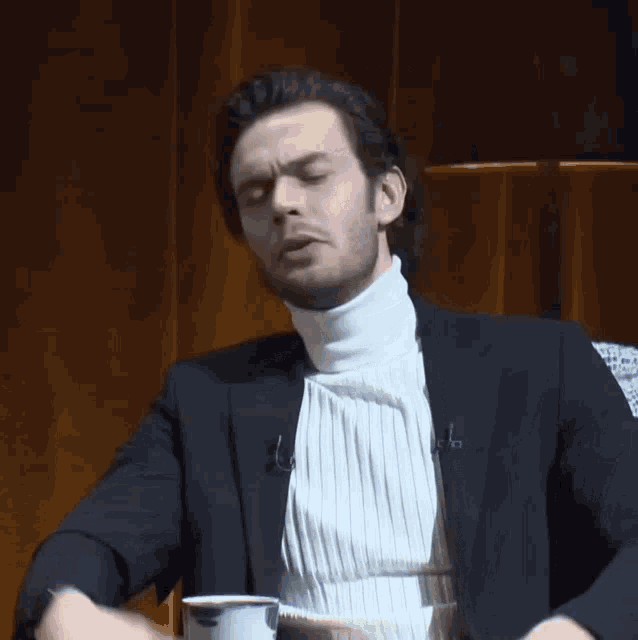 a man wearing a black jacket and a white turtleneck is making a funny face