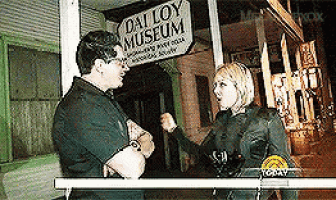 a man and woman are talking in front of a dalroy museum sign .