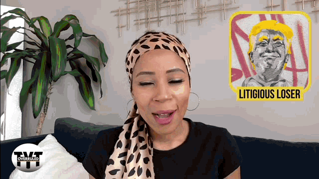 a woman sitting on a couch with a picture of donald trump behind her that says litigious loser