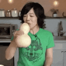 a woman wearing a green shirt with a wolf on it is blowing a balloon .