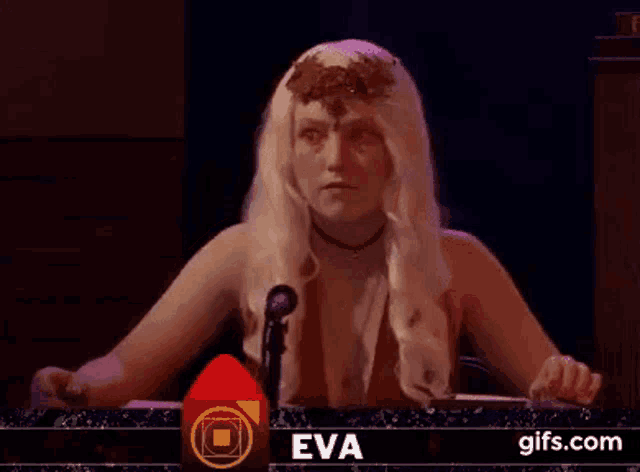 a woman in a wig is sitting at a table with a microphone .