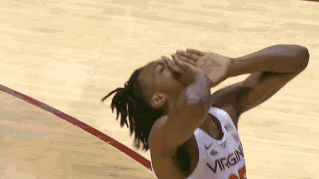 a basketball player wearing a virgin jersey is covering his face with his hands